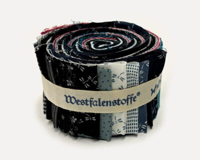 Rolled bundle of patchwork fabric strips in navy, cream, and blue tones bound with a beige ribbon-style band. Close-up of a fabric bolt showing layered quilt-like swatches rolled together and tied with a light beige strap. Assorted fabric samples rolled into a coil, featuring dark and light patterns in blue, black, and red hues. A tightly wound stack of fabric strips forming a circular roll, bound by a woven beige belt with printed text accents. Close-up of a fabric roll used for quilting projects, displaying various printed patterns bound by a neutral strap.