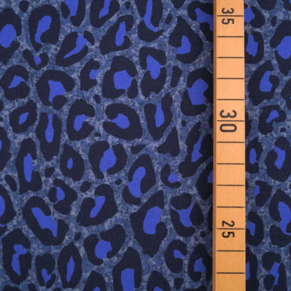 Close-up of blue leopard-print fabric with an orange measuring tape showing around 30 cm.