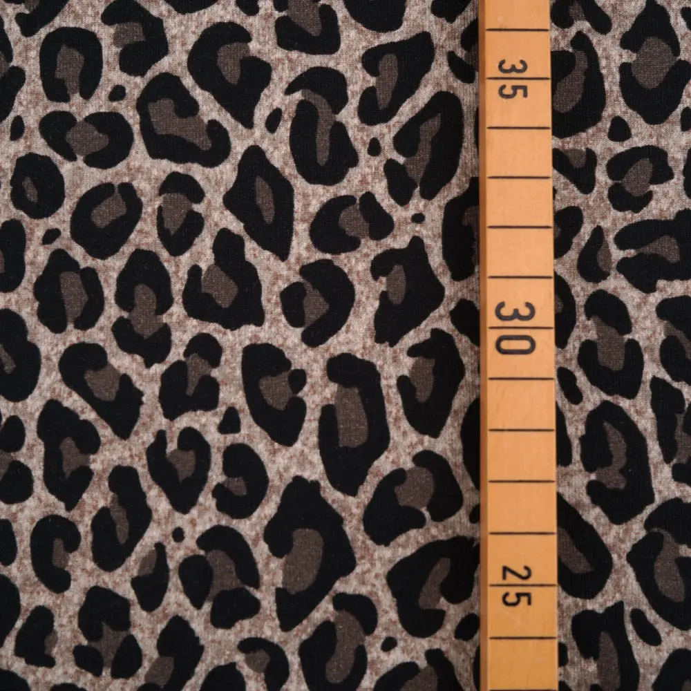 Leopard print fabric with an orange measuring tape laid vertically, showing numbers 25–35.
