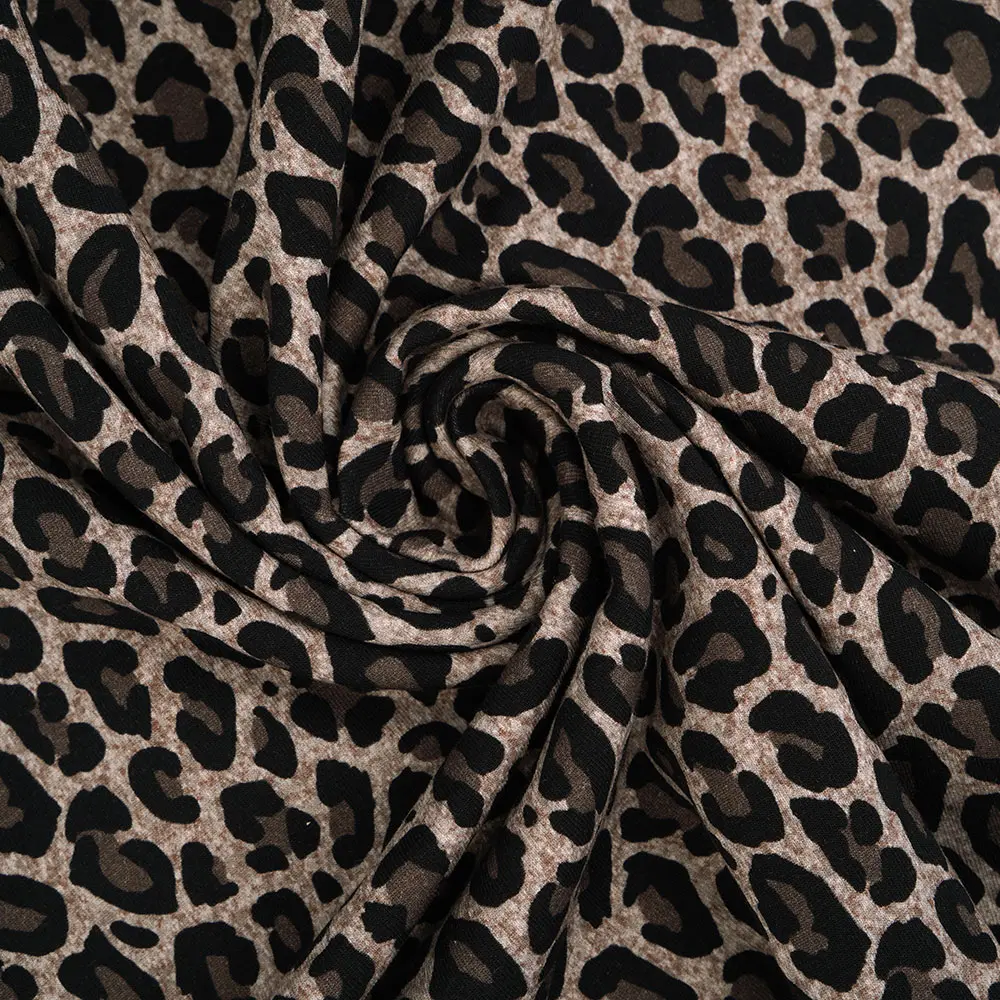Close-up of leopard-print fabric with a tan/beige background and irregular black spots, showing soft folds and texture.
