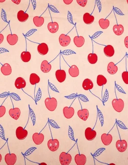Decorative fabric pattern of red and pink cherries with blue stems and leaves on a peach background, some cherries have faces.